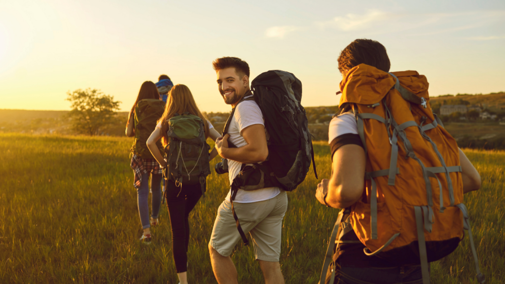 a group of people with backpacks walking through a field at sunset