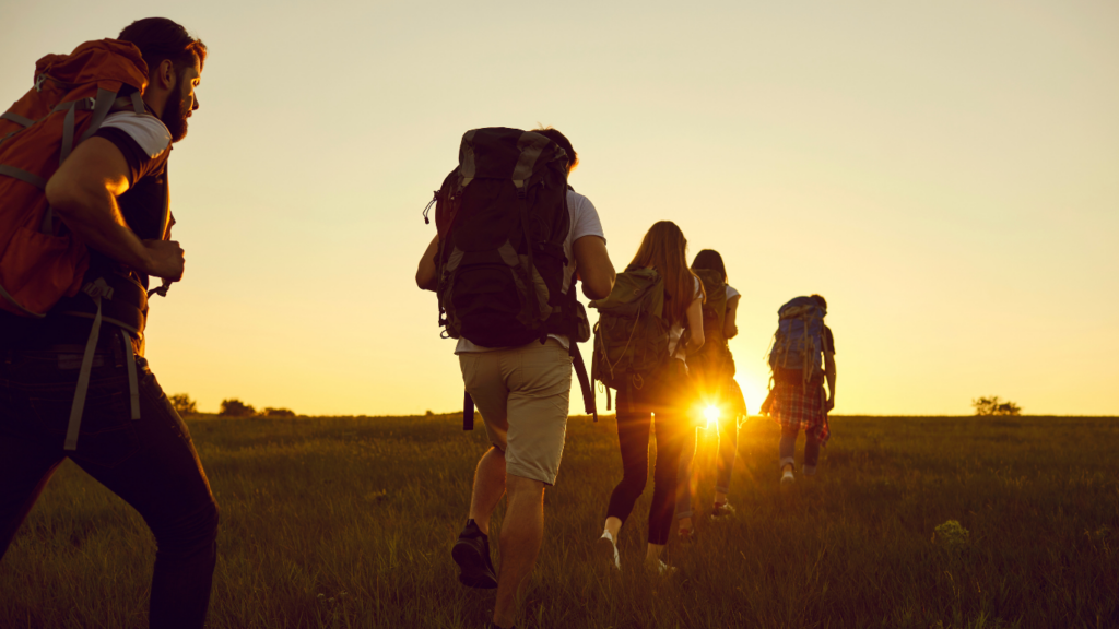 a group of people with backpacks walking through a field at sunset