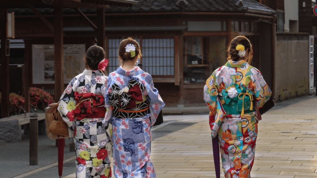 three people dressed in kimono walking down a street