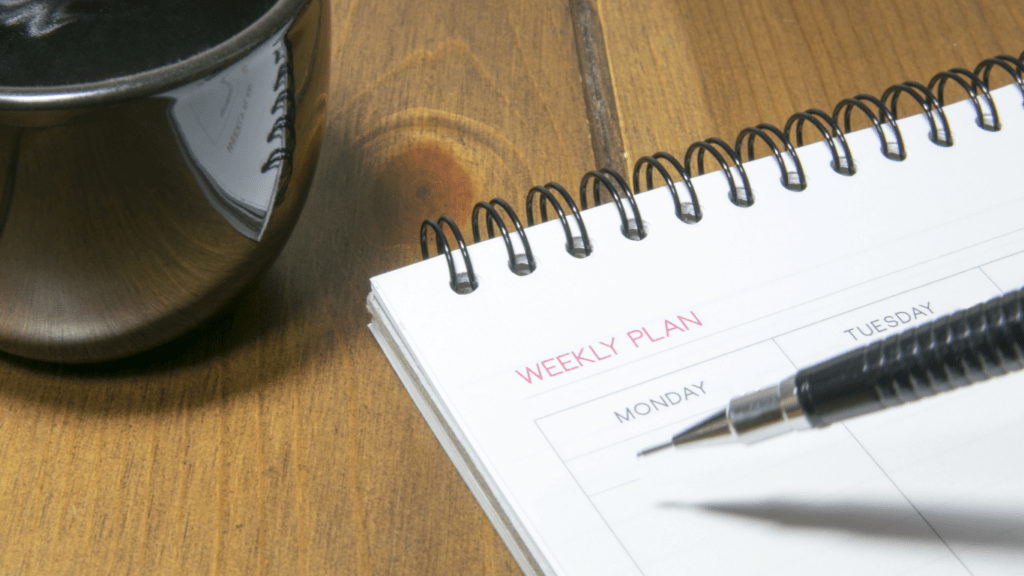 weekly planner with pen and cup of coffee on wooden table